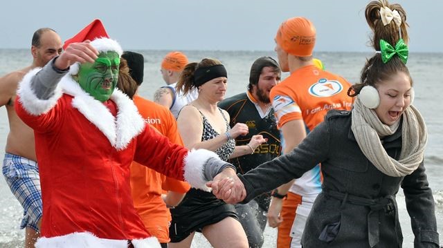 A man dressed up like the Grinch with a Santa Claus suit walks out of a lake during a polar plunge event.