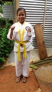 A young girl wearing a karate outfit showing off her medals.