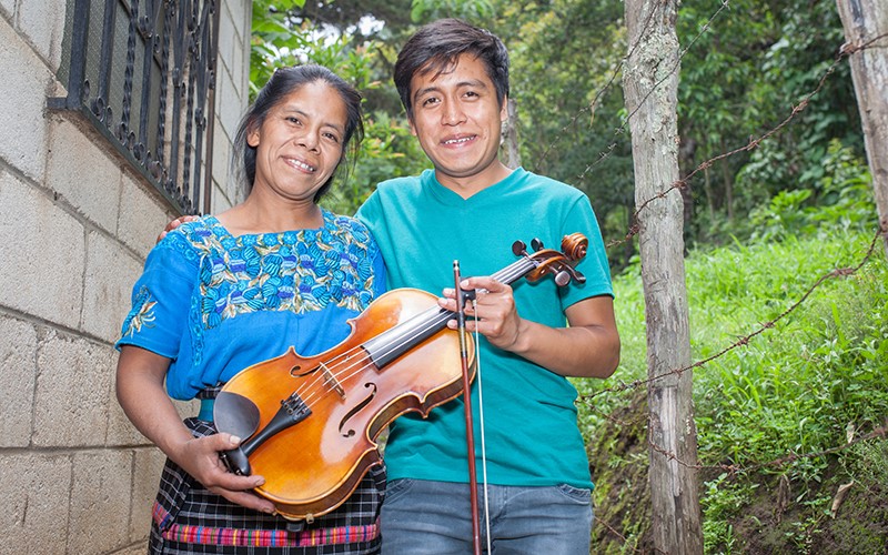 Tomasa and Gustavo hold his viola together outside their home in Guatemala.