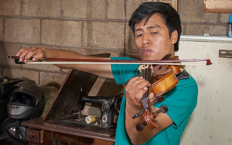 Gustavo, standing in his home, has his viola nestled into his neck in the playing position.
