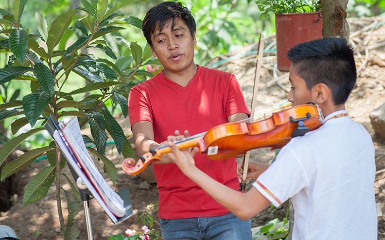 Gustavo teaches a younger male student how to properly hit the right notes on the violin.
