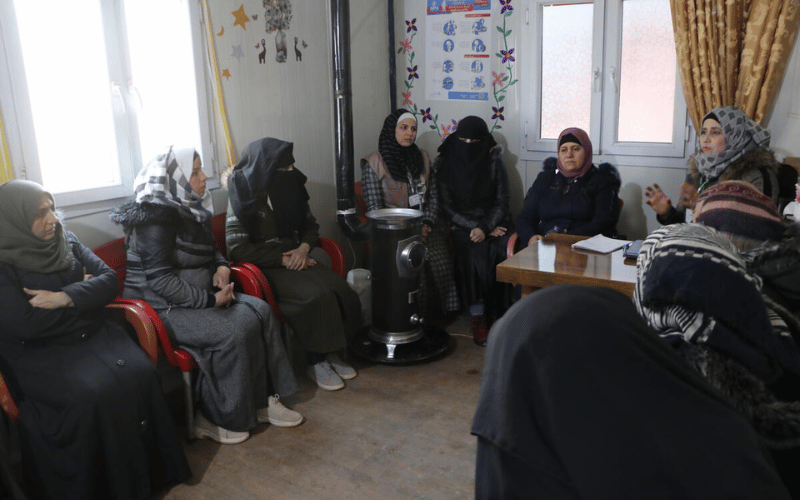 A group of Syrian women sit together in a room, talking.
