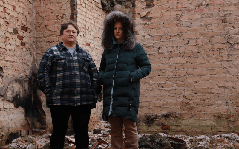 Irina and Zoya stand somberly among the ruins of their house, which was destroyed in the Ukraine conflict.