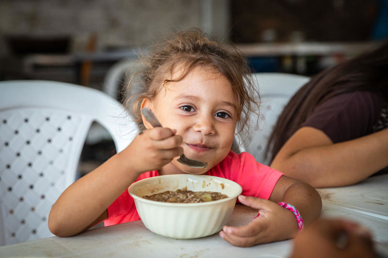 A young Venezuelan girls holds a spoon as she eats her meal.