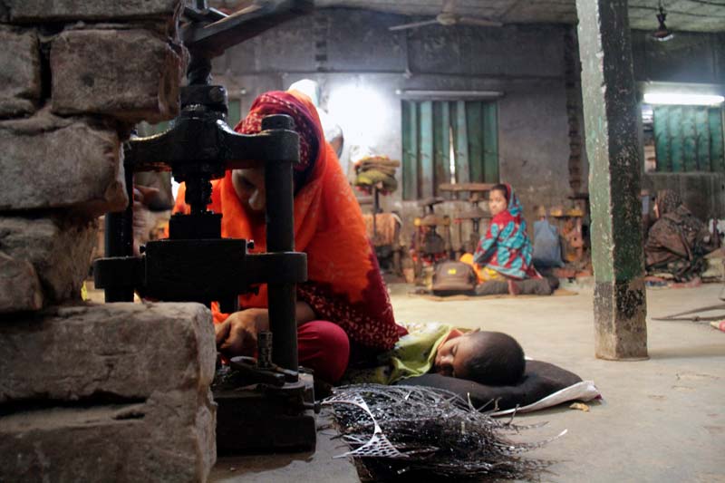 A girl sitting on the floor next to a sleeping child, operating a heavy-duty machine.