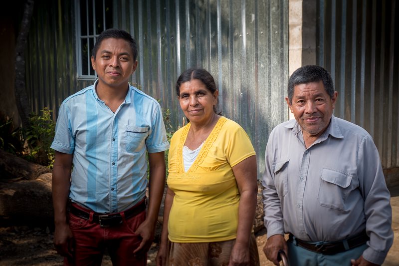 A young man from El Salvador poses for the photo with his mother and father