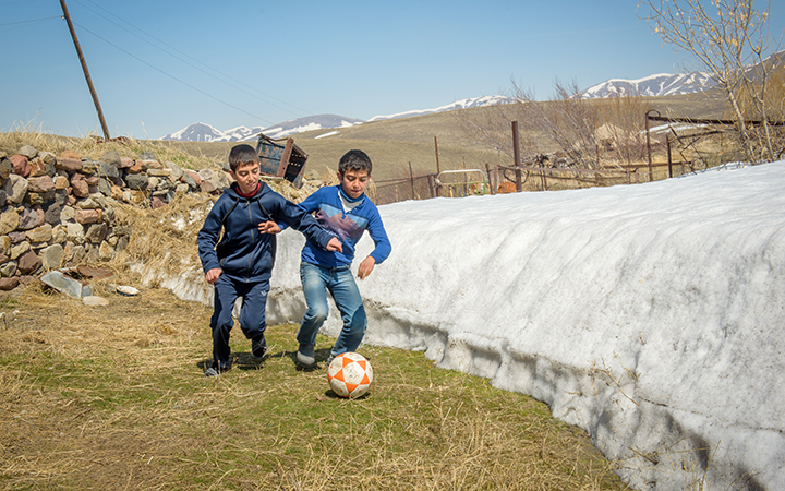 Deux frères jouent avec un ballon de soccer en courant le long d’un amas de neige dans leur village en Arménie.