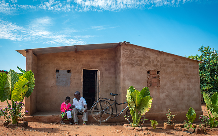 Un père et sa fille lisent un livre ensemble, assis sur le porche de leur maison en Zambie.