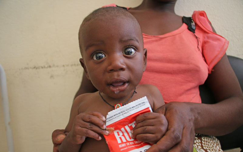 An Angolese baby holds a package of ready-to-use therapeutic food. He is held by this mother.