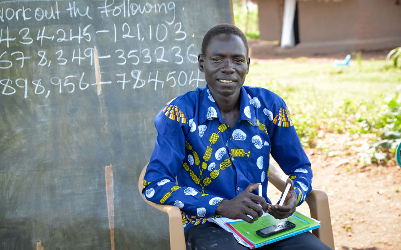 A South Sudanese man sits in front of a chalkboard