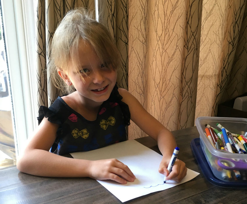 A little girl sits at the table, smiling and colouring