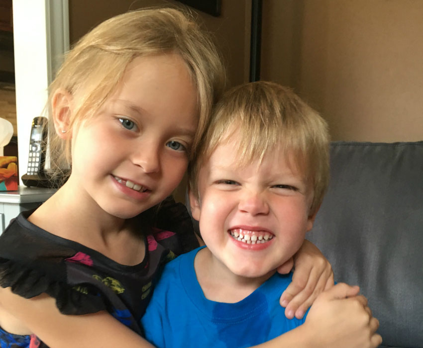 A blonde girl hugs her little brother