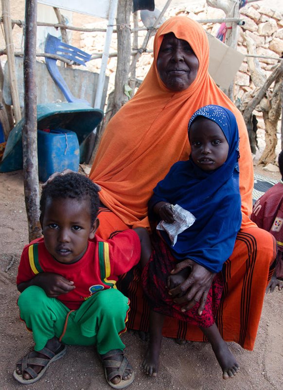 A Somali woman sits with two toddlers. The girl child holds a white package of ready-to-use-therapeutic-food (RUTF)