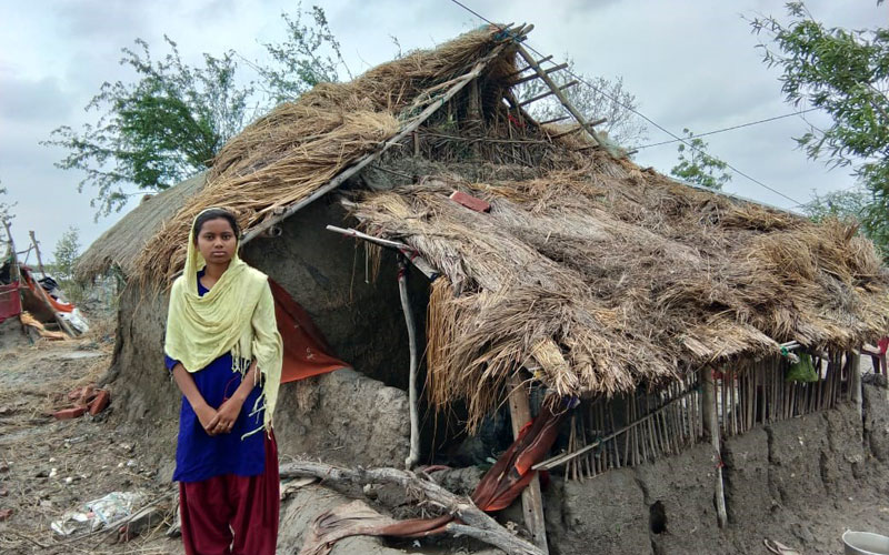 a young Indian girl stands in front of a shelter