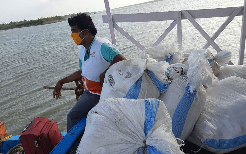 an Indian man sits on the edge of a boat that is piled high with white sacs filled with emergency supplies