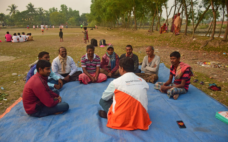 a group of Indian men sit on mats on the ground