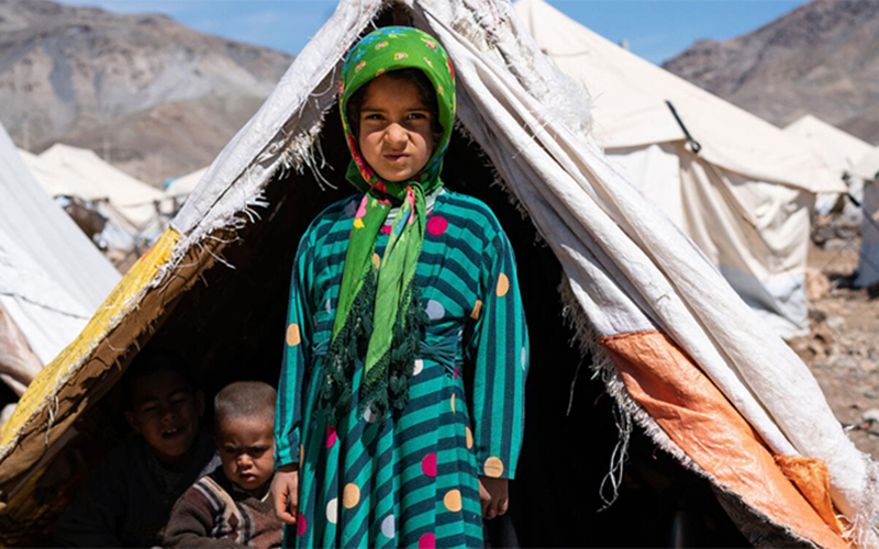A young girl from Afghanistan stands in front of tent in a refugee camp.