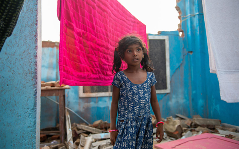 a girl from India stands outside the ruins of her school, destroyed by Cyclone Fani in 2019.