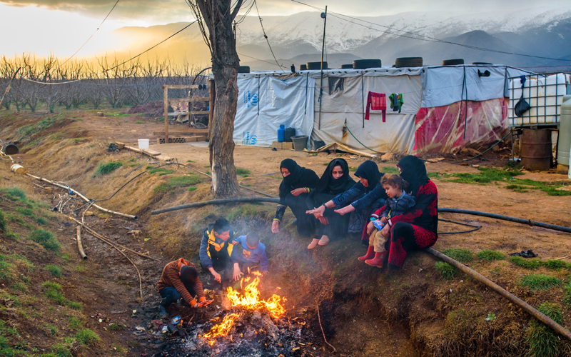 Women and children from Syria sit around a bonfire at a refugee camp.