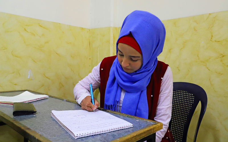 A Syrian teen girl writes on a notebook as she studies.
