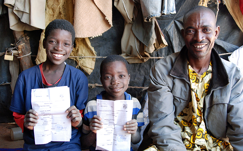 Two school-age boys in Mali hold up their birth certificates, smiling broadly.