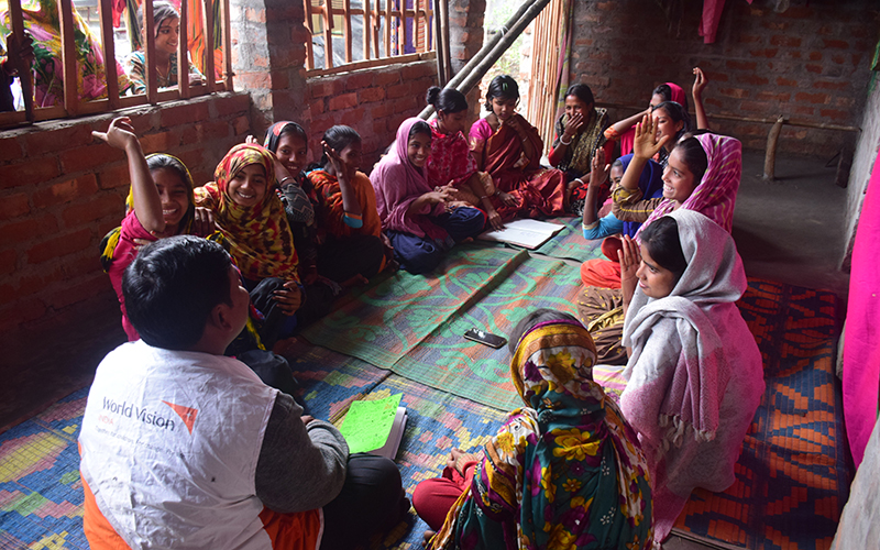 A group of adolescent girls sits in a circle, looking toward a World Vision leader.