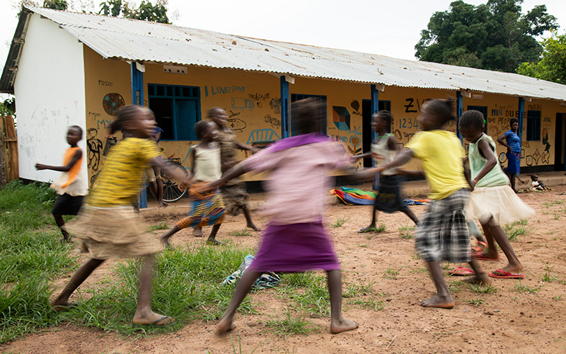 In South Sudan, a group of adolescent and teen girls plays in a circle, holding hands. Some are laughing.