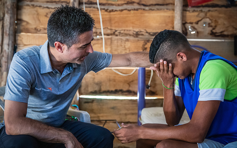 A 16-year-old boy cries while talking with a World Vision worker, who is comforting him.
