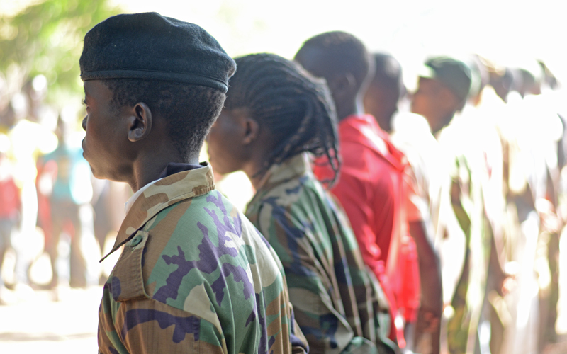 A line of children dressed in fatigues, photographed from behind.