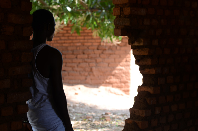 A young man, former child soldier in South Sudan, leans against a broken brick wall.