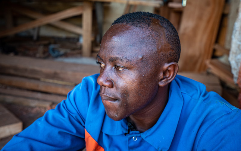 A young man from DRC wears  a blue shirt and looks left.