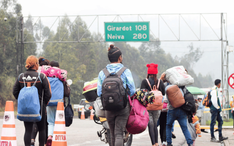 A crowd of migrants carry backpacks and bags as they walk across a highway.