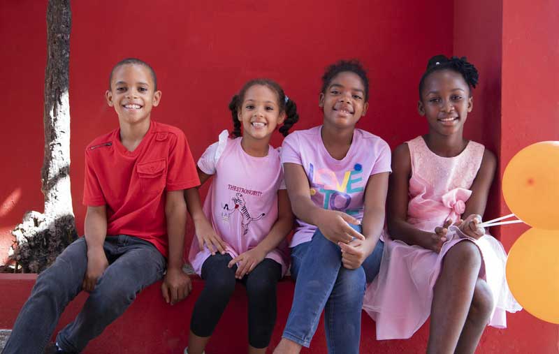 A boy and three girls from the Dominican Republic sitting on a red bench.