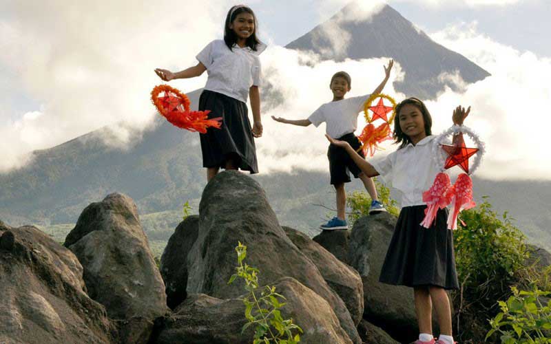 Two girls and a boy holding festive decorations stand on large rocks.