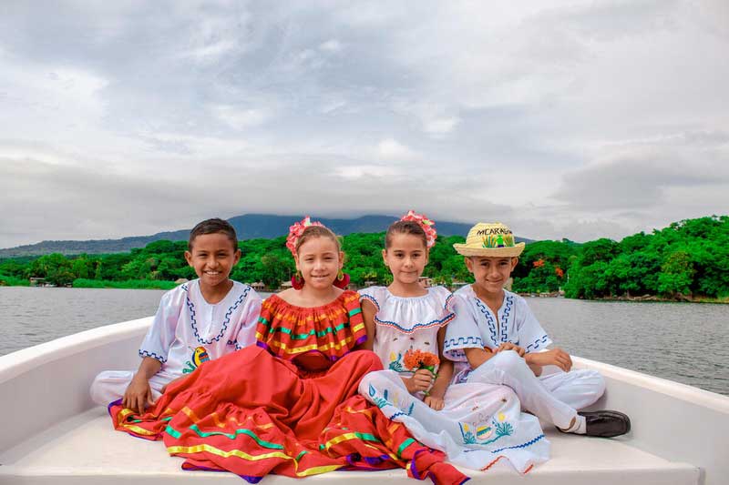 Four children wearing traditional clothes from Nicaragua sit on a boat.