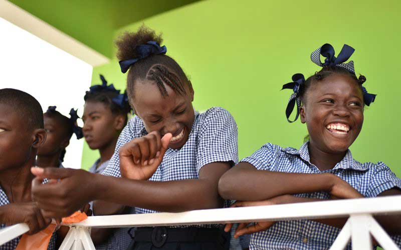 Three Haitian school aged girls smile and laugh.