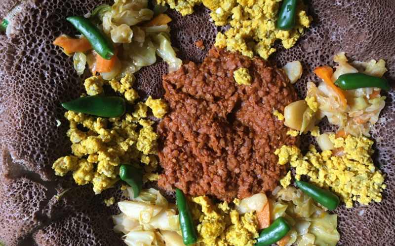 a plate covered in Ethiopian ijera, veggies and eggs.
