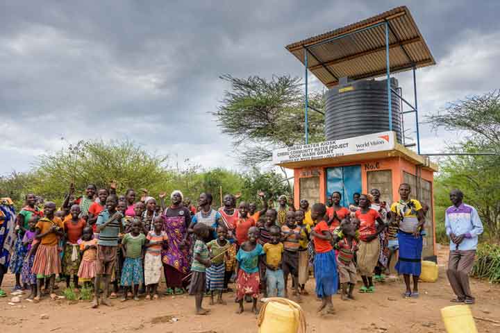 A large group of people stand in front of a water collection kiosk installed in a village in Kenya.