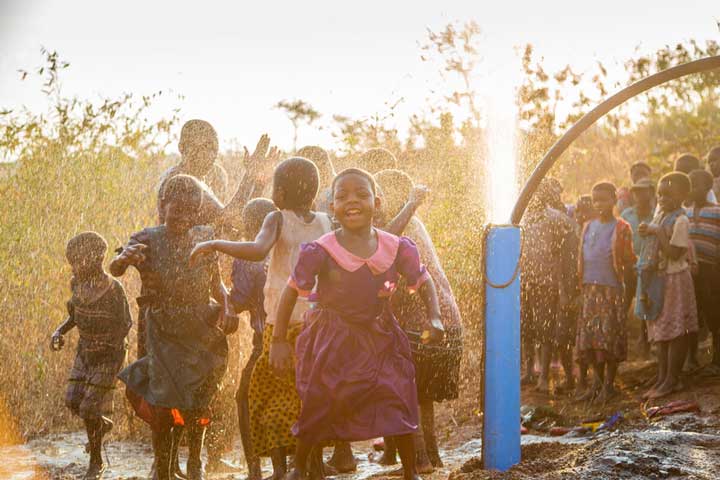 Children sing and dance under the spray of water bursting up from the ground.