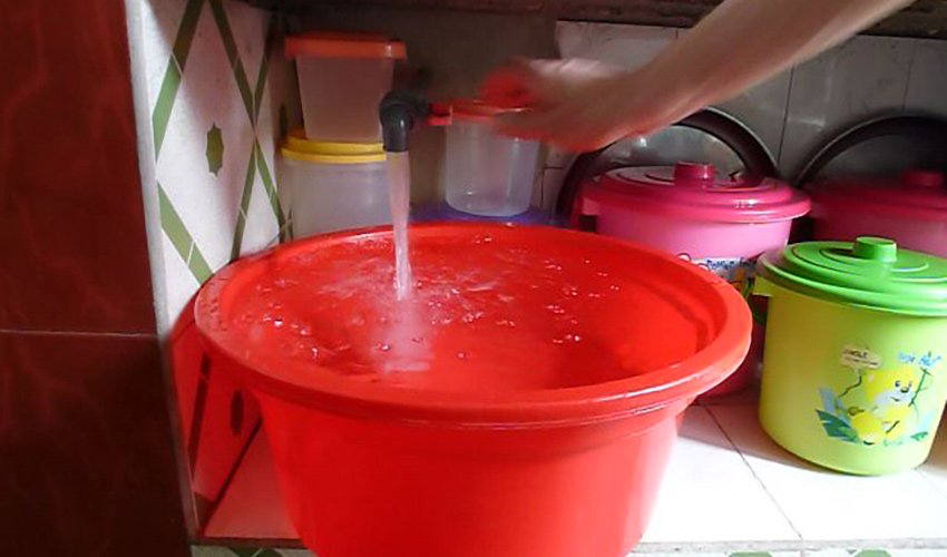 a hand turns on a tap to fills up a red bucket with water