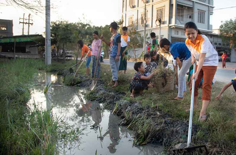 A group of children and young people clean a stream using rakes and hoes.