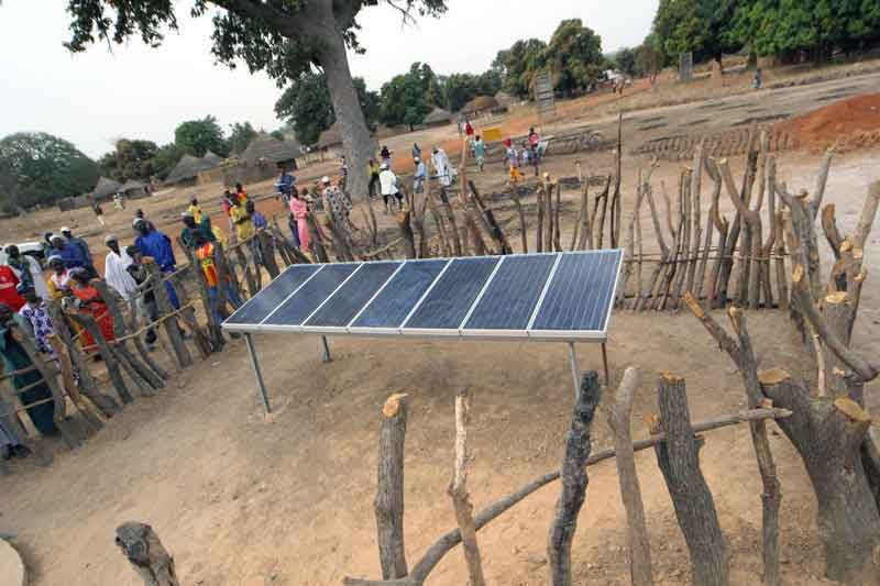 A solar panel surrounded by a stick fence stands in the heart of a community in Senegal.