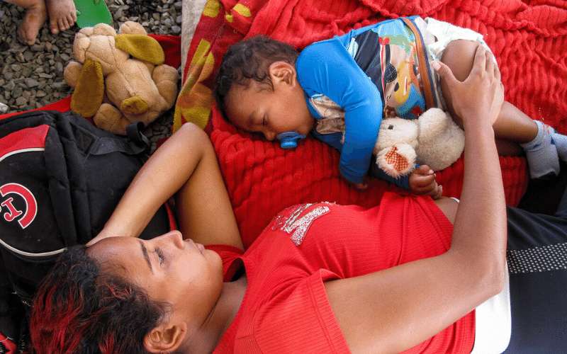 A mother and child rest on some blankets spread on the ground.