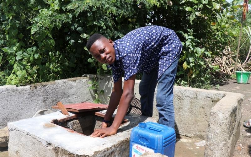 Tejan in Sierra Leone bends over a freshwater well, with a bucket beside him.