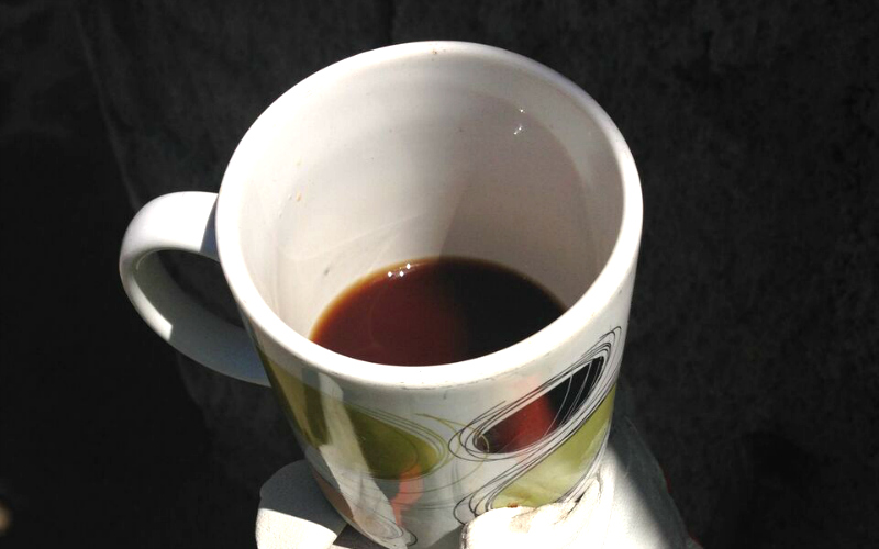 a mug of dark coffee held in gloved hands