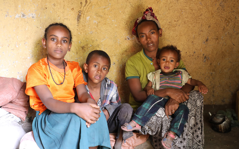 Trois enfants éthiopiens sont assis à côté d’un mur jaune avec leur mère