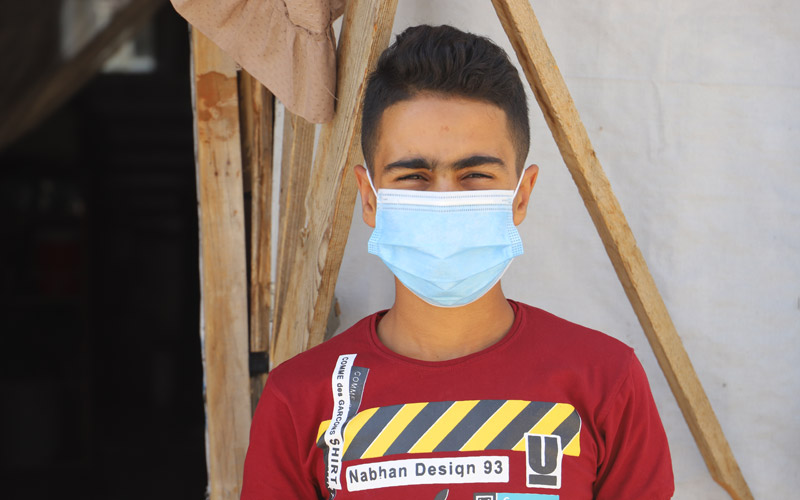 Un garçon syrien porte un masque et se tient devant une tente