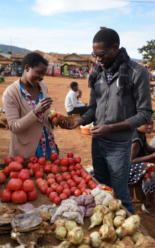 A man is buying food from a woman at a market in Beni, DRC.