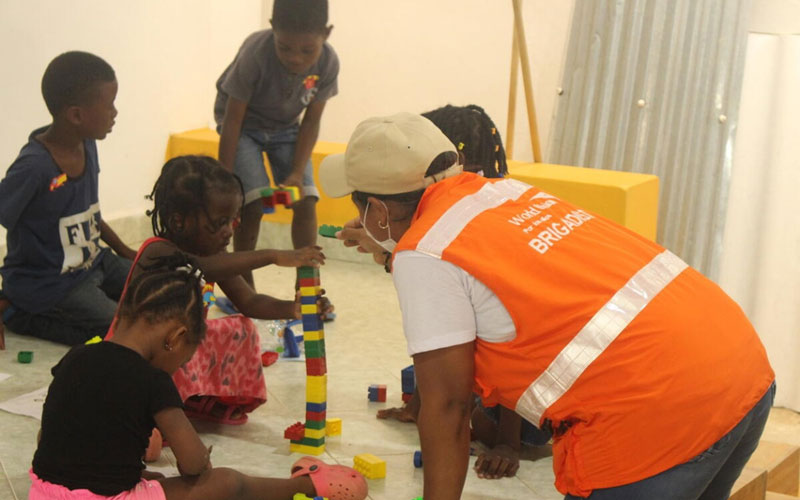 A woman in a World Vision vest kneels to build Lego with children.