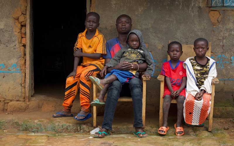 A father and his four children, displaced from their community in the Central African Republic, sit outside a mud hut.